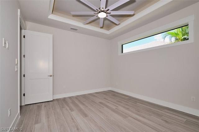 empty room with a wealth of natural light, ceiling fan, light hardwood / wood-style floors, and a raised ceiling