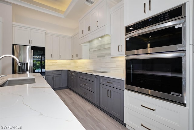 kitchen with backsplash, white cabinetry, light wood-type flooring, appliances with stainless steel finishes, and sink