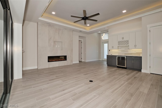 unfurnished living room with beverage cooler, light hardwood / wood-style floors, a tiled fireplace, and a raised ceiling