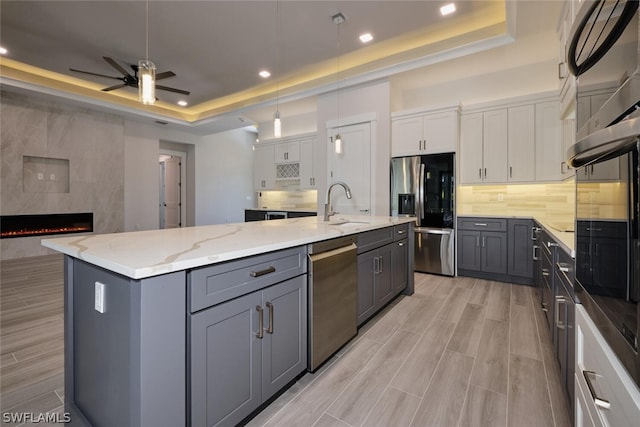 kitchen with white cabinetry, a tile fireplace, a center island with sink, and a raised ceiling