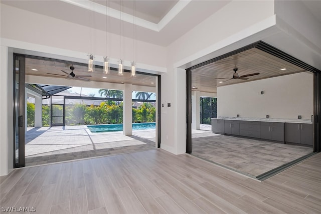 interior space with ceiling fan, a tray ceiling, and light hardwood / wood-style flooring