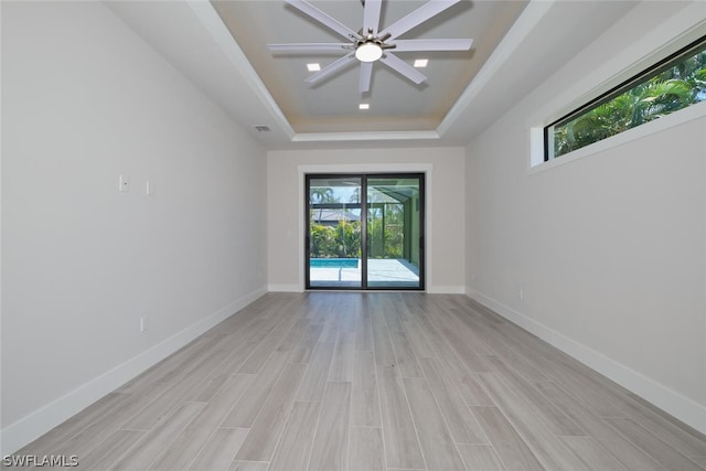 empty room featuring ceiling fan, a tray ceiling, and light hardwood / wood-style flooring