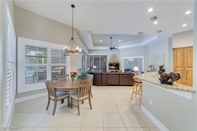 dining room featuring ceiling fan with notable chandelier, a raised ceiling, a healthy amount of sunlight, and light tile flooring