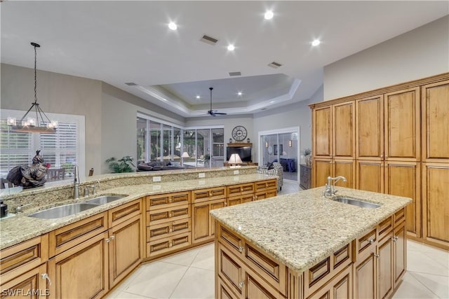 kitchen with a tray ceiling, open floor plan, a kitchen island with sink, and a sink