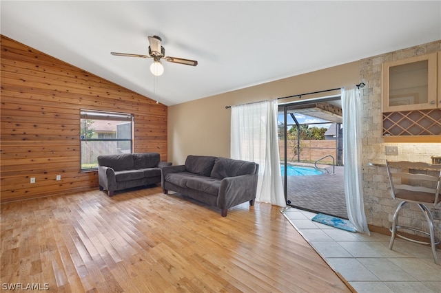 living room with ceiling fan, lofted ceiling, wood walls, and light wood-type flooring