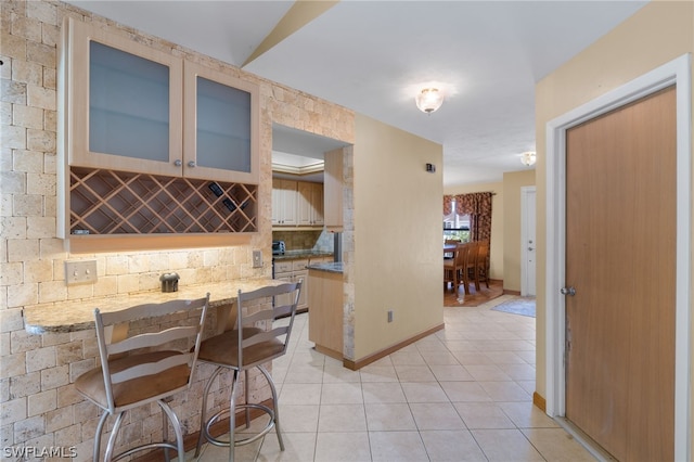 kitchen featuring a breakfast bar area, light stone counters, backsplash, and light tile floors