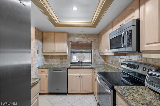 kitchen featuring appliances with stainless steel finishes, dark stone counters, sink, light brown cabinetry, and a raised ceiling