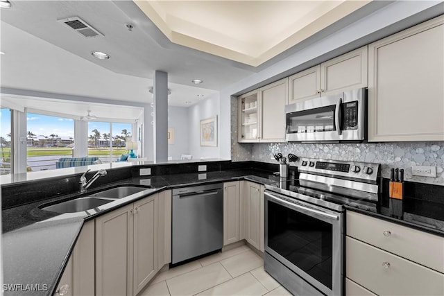 kitchen featuring sink, light tile patterned floors, appliances with stainless steel finishes, dark stone countertops, and decorative backsplash