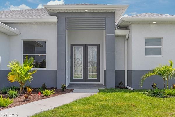 property entrance with stucco siding, a shingled roof, a lawn, and french doors