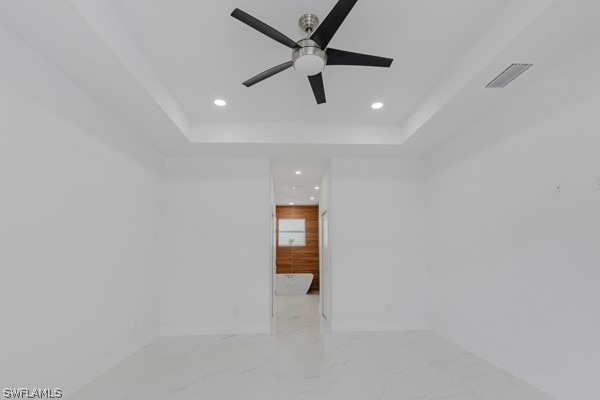 tiled empty room featuring ceiling fan and a tray ceiling