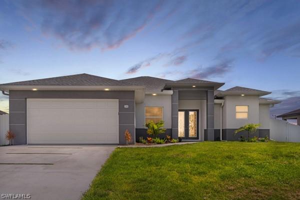 prairie-style house with a garage, concrete driveway, a yard, and stucco siding