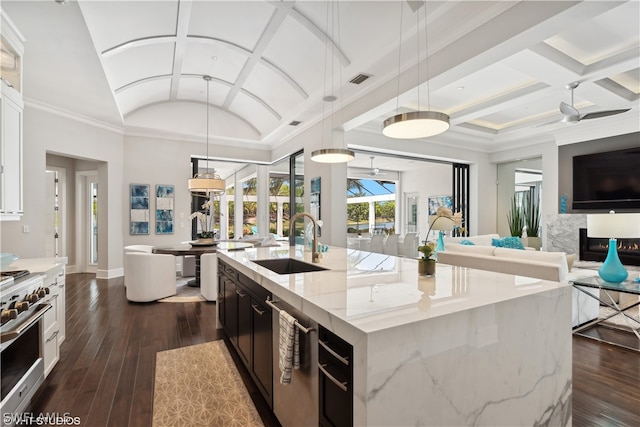 kitchen featuring sink, stainless steel stove, hanging light fixtures, light stone countertops, and an island with sink