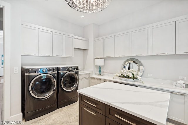 clothes washing area with cabinets, a chandelier, and independent washer and dryer