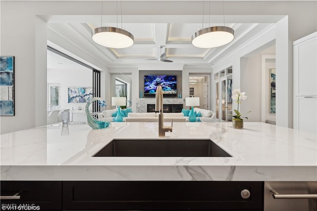 kitchen with pendant lighting, coffered ceiling, light stone countertops, and sink