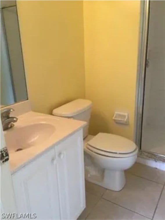 bathroom featuring a shower with door, tile flooring, toilet, and vanity with extensive cabinet space