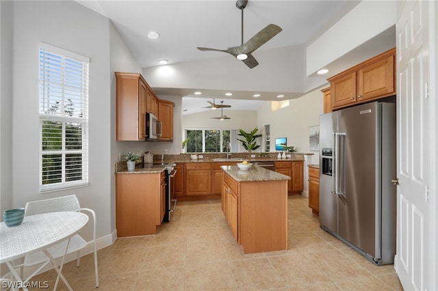 kitchen featuring kitchen peninsula, appliances with stainless steel finishes, light stone counters, a kitchen island, and lofted ceiling