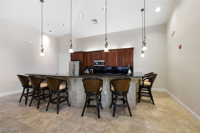 kitchen with hanging light fixtures, stainless steel appliances, a kitchen breakfast bar, high vaulted ceiling, and light tile patterned floors