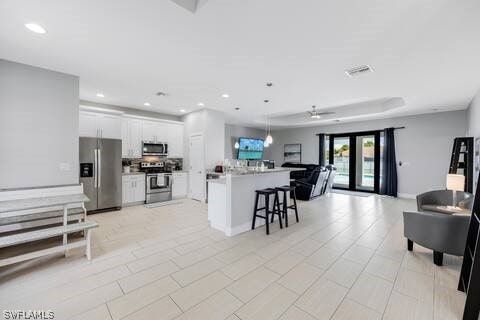 kitchen featuring ceiling fan, kitchen peninsula, white cabinetry, stainless steel appliances, and a kitchen bar