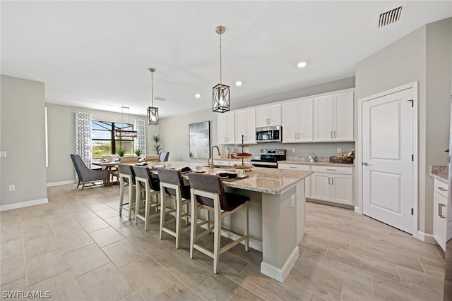 kitchen with hanging light fixtures, appliances with stainless steel finishes, white cabinetry, and a kitchen island with sink