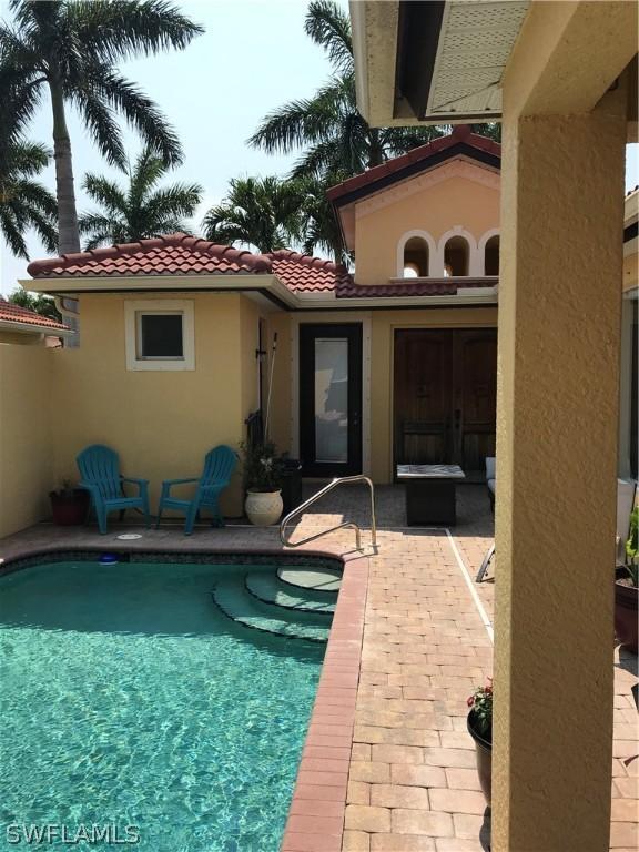 rear view of property featuring stucco siding, a patio, a tile roof, and an outdoor pool