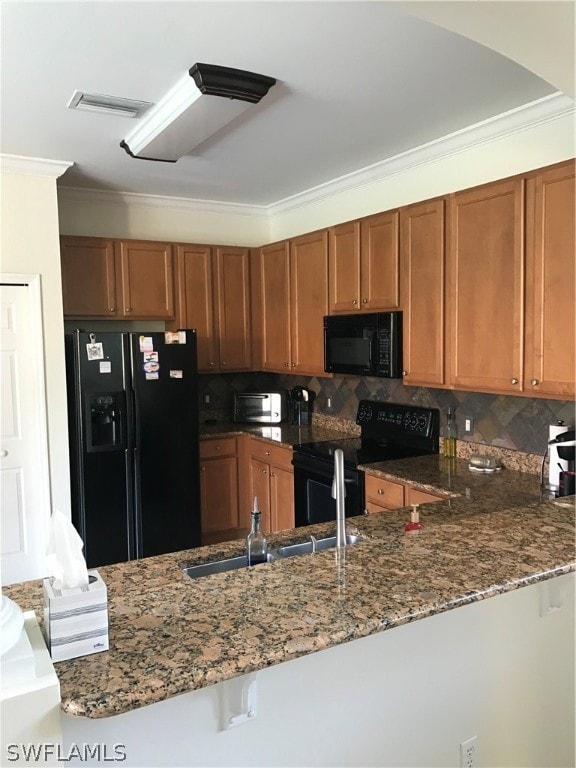 kitchen with dark stone countertops, black appliances, tasteful backsplash, and crown molding