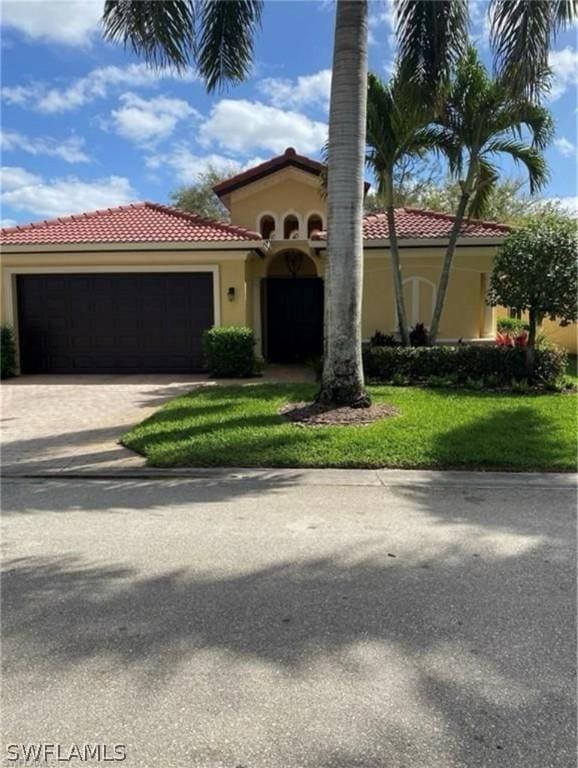 mediterranean / spanish-style house featuring a tile roof, a front lawn, a garage, stucco siding, and driveway