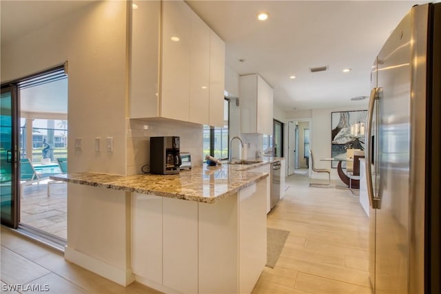 kitchen featuring light stone countertops, appliances with stainless steel finishes, white cabinets, and kitchen peninsula