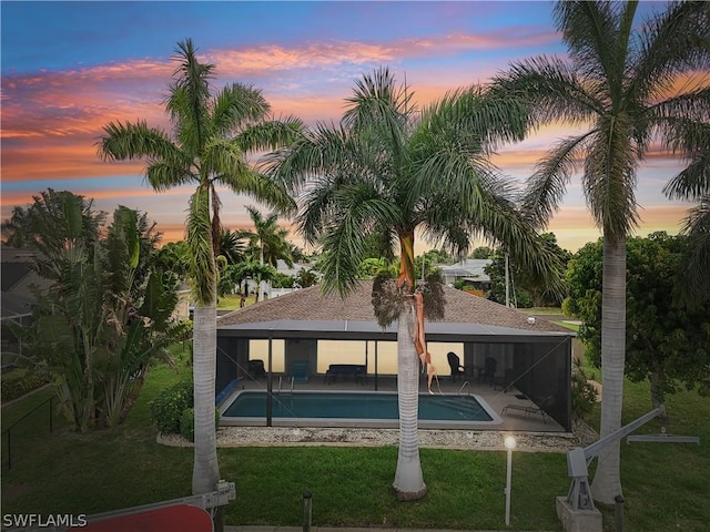 pool at dusk featuring glass enclosure, a yard, and a patio