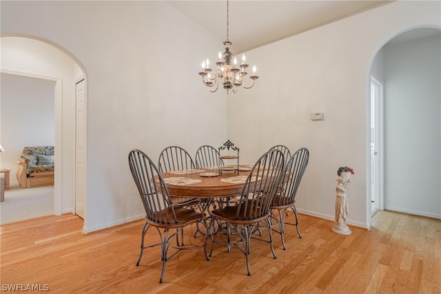 dining space with a notable chandelier, light wood-type flooring, and vaulted ceiling