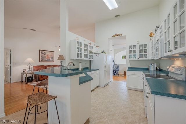 kitchen featuring light tile flooring, kitchen peninsula, a kitchen breakfast bar, white cabinets, and white appliances