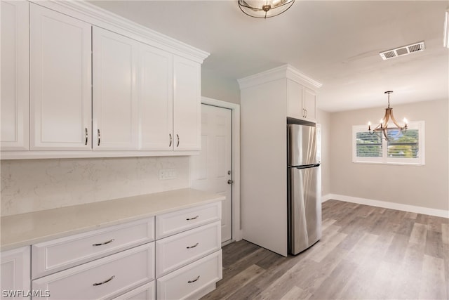 kitchen with wood-type flooring, white cabinetry, hanging light fixtures, and stainless steel refrigerator