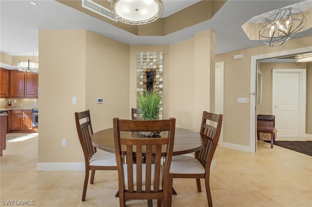 dining room with a raised ceiling, light tile floors, and an inviting chandelier