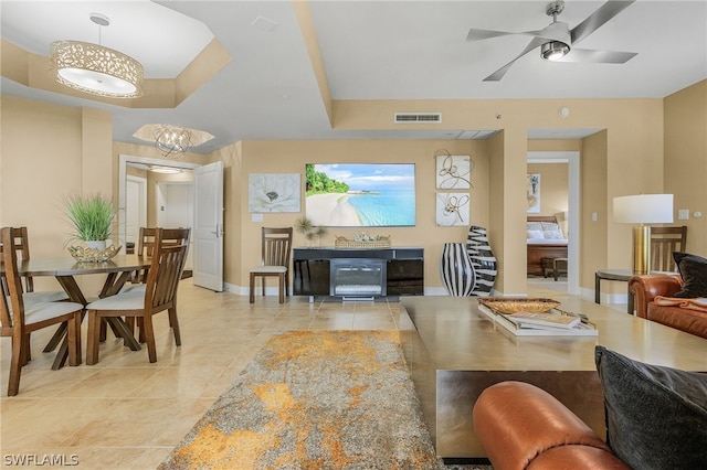 living room featuring a raised ceiling, ceiling fan with notable chandelier, and light tile floors