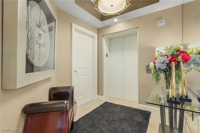 foyer featuring tile flooring, a raised ceiling, and elevator