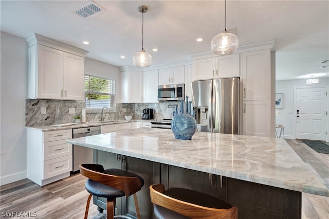 kitchen with a kitchen bar, stainless steel appliances, light stone countertops, and white cabinetry