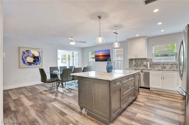 kitchen featuring a center island, light stone countertops, appliances with stainless steel finishes, light hardwood / wood-style floors, and white cabinetry