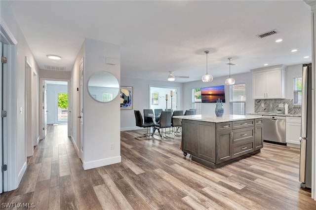 kitchen with light hardwood / wood-style flooring, stainless steel appliances, a center island, ceiling fan, and decorative backsplash