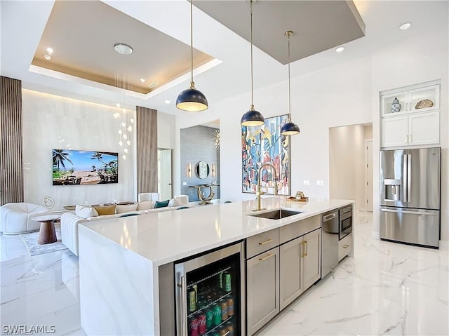 kitchen with pendant lighting, sink, appliances with stainless steel finishes, a tray ceiling, and beverage cooler