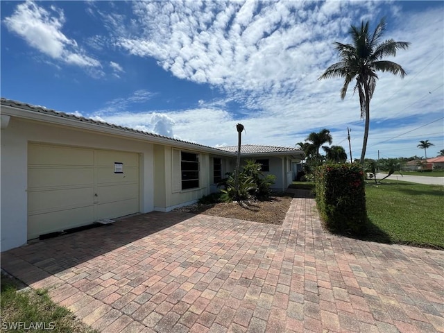 ranch-style house with a garage, decorative driveway, a tile roof, and stucco siding