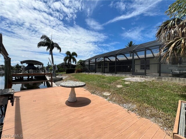 deck featuring a water view, a boat dock, glass enclosure, and a lawn