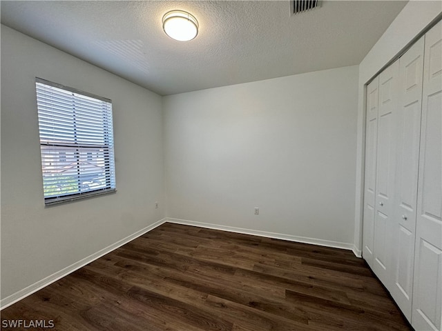 unfurnished bedroom featuring a closet, a textured ceiling, and dark hardwood / wood-style floors