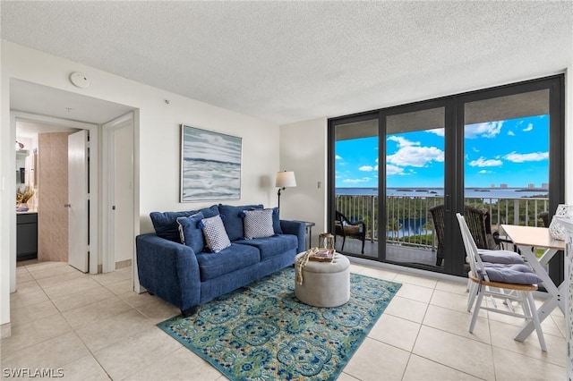 living room with a water view, light tile patterned floors, a textured ceiling, and a wall of windows