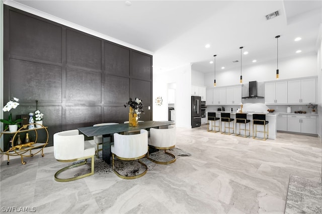 interior space with a large island with sink, wall chimney exhaust hood, a kitchen breakfast bar, decorative light fixtures, and white cabinetry