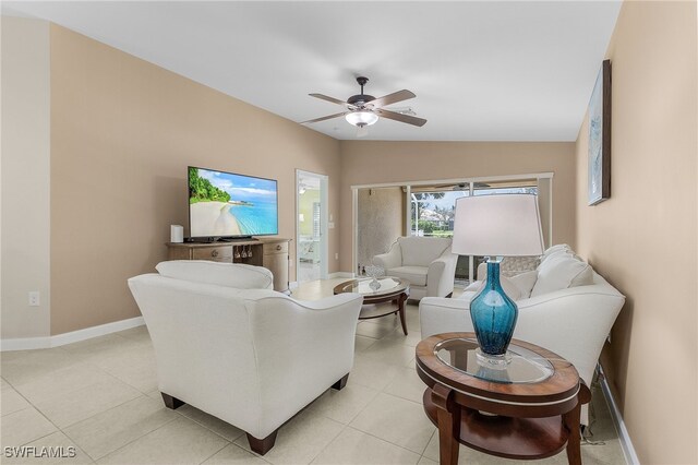 living area with lofted ceiling, light tile patterned floors, a ceiling fan, and baseboards