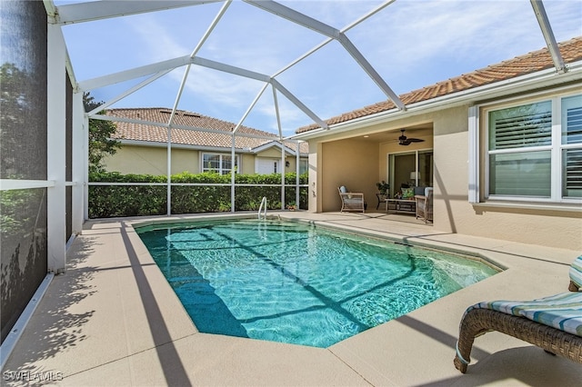 outdoor pool with glass enclosure, a patio area, and ceiling fan