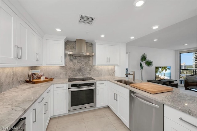 kitchen featuring appliances with stainless steel finishes, light stone counters, wall chimney exhaust hood, sink, and white cabinets