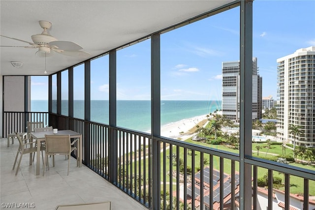 unfurnished sunroom with ceiling fan, a water view, and a beach view