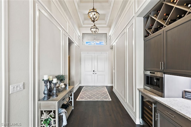 mudroom with dark wood-type flooring, a towering ceiling, wine cooler, a notable chandelier, and ornamental molding