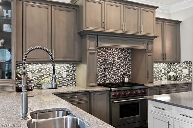 kitchen with sink, crown molding, high end stainless steel range oven, light stone counters, and decorative backsplash