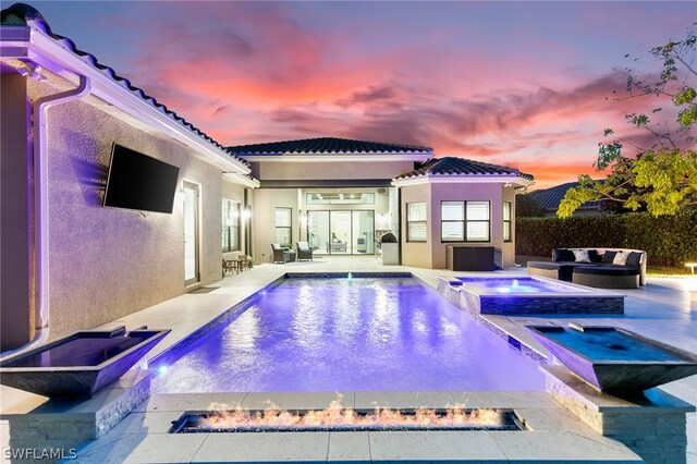 pool at dusk with an in ground hot tub and a patio area